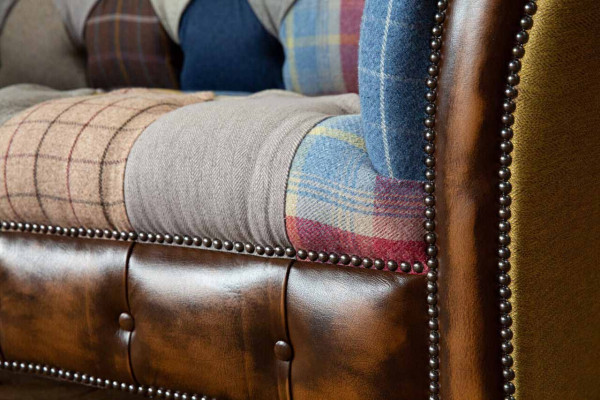 Chesterfield sofa z textilu a kůže na nohách z přírodního dřeva.