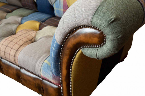Chesterfield sofa z textilu a kůže na nohách z přírodního dřeva.
