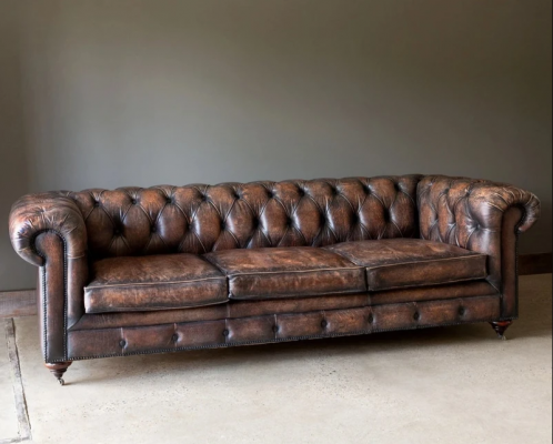 Hnědá pohovka Chesterfield se třemi sedadly a koženým potahem v anglickém stylu.