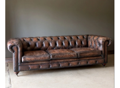 Hnědá pohovka Chesterfield se třemi sedadly a koženým potahem v anglickém stylu.