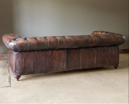 Hnědá pohovka Chesterfield se třemi sedadly a koženým potahem v anglickém stylu.